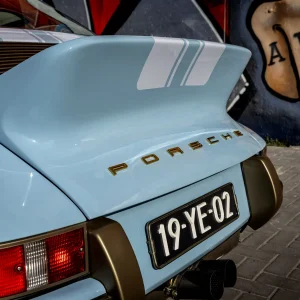 Blue Porsche 911 Targa rear with racing stripes, gold lettering, taillight, and dual exhausts.